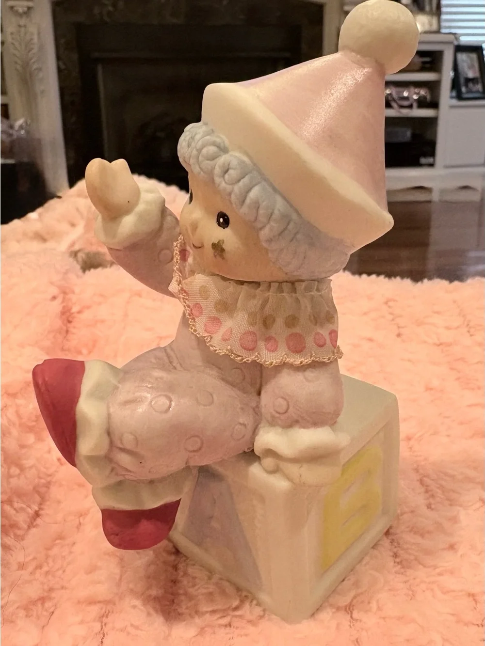 Hand -painted pastel pink-clad baby clown wearing a textured hat.